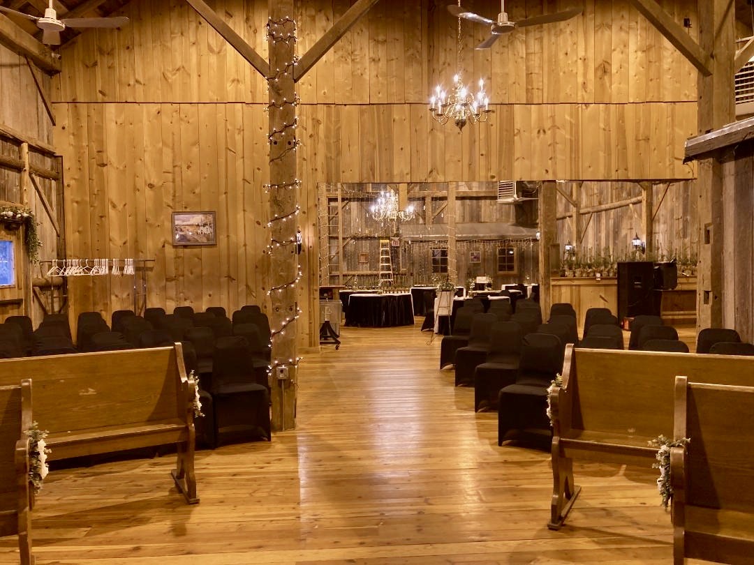 Event barn interior with chandeliers and wooden pews set for ceremony
